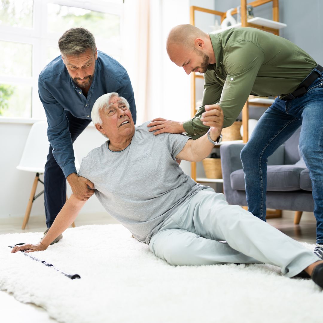 an older adult on the floor and two people helping him