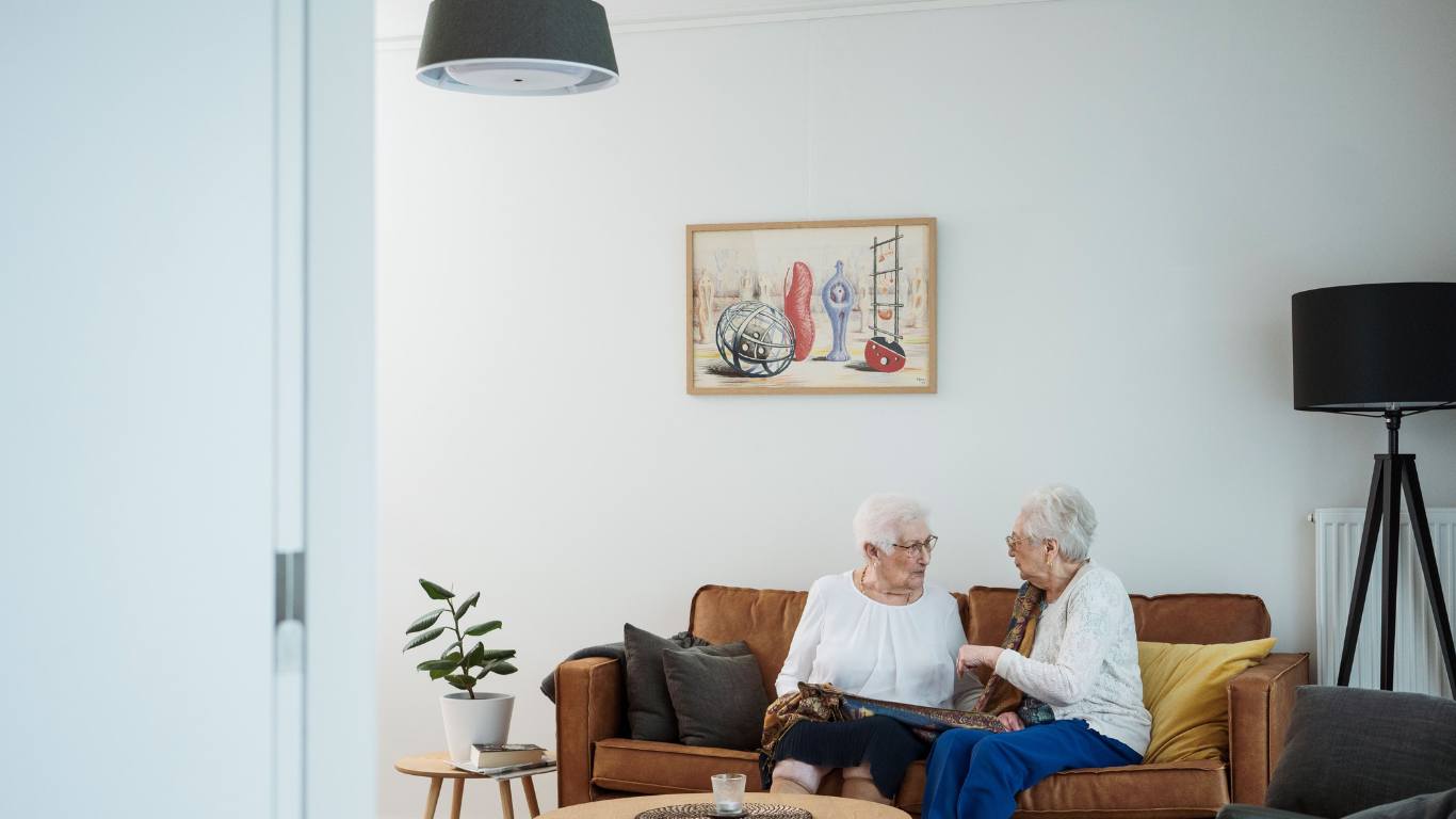 Two older women sitting on a sofa with the nobi lamp